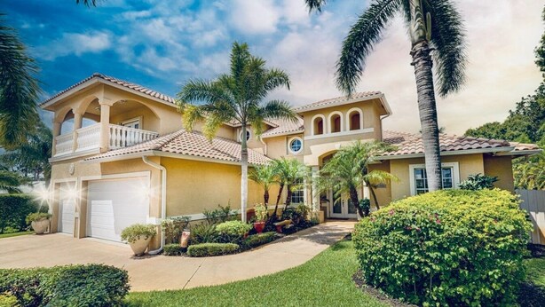 A two-story house with a covered patio, a garage, and a well-maintained garden with palm trees and shrubs. - Private Villa | Heated Pool + Hot Tub + Sleeps 20 (Port St. Lucie)