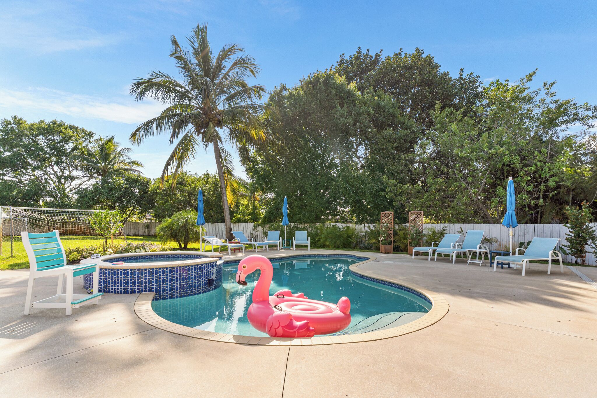 A swimming pool with a pink flamingo float, lounge chairs, and a hot tub.