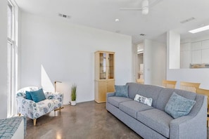 A modern living room with a grey sofa, a patterned armchair, a wooden cabinet, and a small table with a plant. - Kingfisher – Modern inside, gorgeous outside (Alpine)