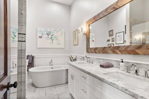 A modern bathroom with a freestanding bathtub, a large mirror, and a marble countertop.