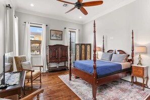A bedroom with a four-poster bed, a wooden desk, a chair, and a ceiling fan.