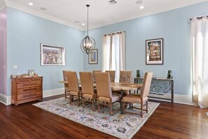 A dining room with a wooden table and chairs, a patterned rug, and framed pictures on the walls.