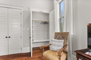 Ein Zimmer mit Holzboden, einem Stuhl mit Kissen, einem Kleiderschrank und einem Fenster mit Vorhängen.