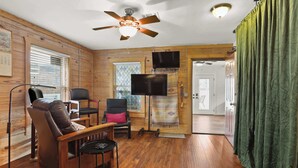 A cozy cabin interior with wooden walls, a ceiling fan, a flat-screen TV, and a wooden dining table with chairs.