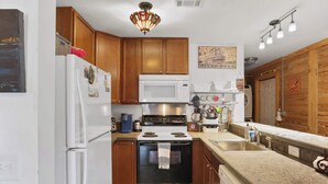 A compact kitchen with wooden cabinets, a white refrigerator, a microwave, a stove, and a sink.