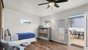 A compact room with a bed, a small table, and a ceiling fan.