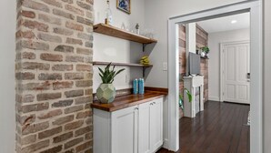Une cuisine avec des meubles blancs, un mur en briques, des étagères en bois et un plan de travail en bois.