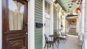 Eine Veranda mit einer Holztür, einem kleinen Tisch mit Stühlen und einem überdachten Bereich mit Geländer.