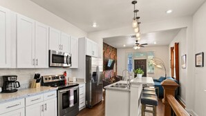 A modern kitchen with white cabinets, stainless steel appliances, and a bar area with stools.