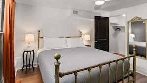 A neatly arranged bedroom with a bed, bedside lamps, a ceiling fan, a wardrobe, and a mirror.