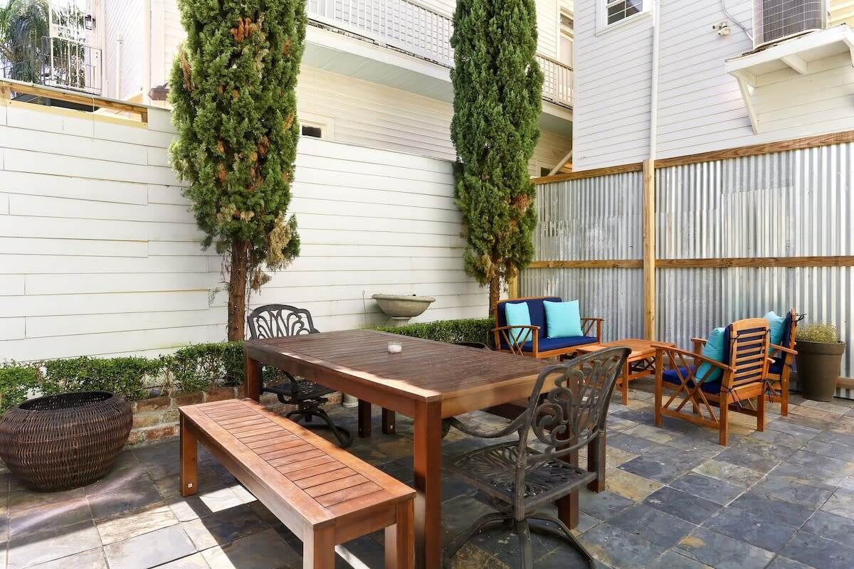 An outdoor patio with a wooden table and benches, surrounded by chairs and a decorative tree.