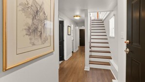 A hallway with a staircase, a framed architectural drawing on the wall, and a door with a brass handle.
