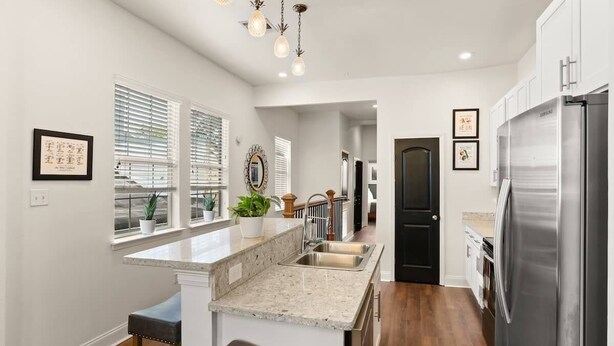 A modern kitchen with a stainless steel refrigerator, granite countertops, and a built-in island with bar stools.