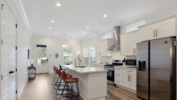 A modern kitchen with white cabinetry, a stainless steel refrigerator, and a central island with bar stools.