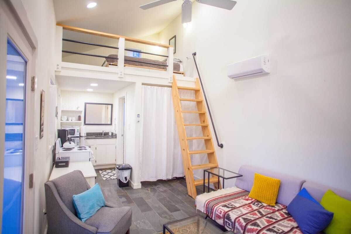 Un espacio habitable compacto con un entrepiso de dormitorio, una kitchenette, un sofá y una escalera al camarote superior.