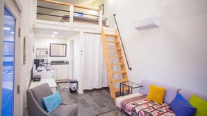 Un espace de vie compact comprenant une chambre en mezzanine, un coin cuisine, un canapé et une échelle menant au lit supérieur.
