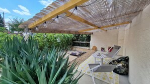 A covered patio area with a pergola, outdoor seating, and a garden.