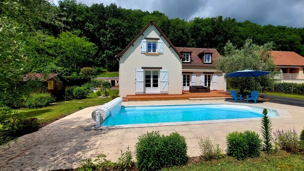 A two-story house with a swimming pool, surrounded by lush greenery and a cloudy sky.