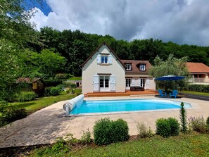 Uma casa de dois andares com piscina, rodeada por vegetação exuberante e um céu nublado.