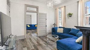 Ein Wohnzimmer mit einem blauen Sofa, einem Glastisch, einer Deckenleuchte und einem Fernseher.