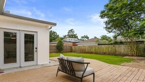 Une terrasse en bois avec un canapé, une porte-fenêtre coulissante et une cour arrière verdoyante.
