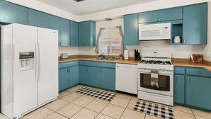 Une cuisine avec des armoires de couleur turquoise, un réfrigérateur blanc, un four à micro-ondes, une cuisinière et un lave-vaisselle.