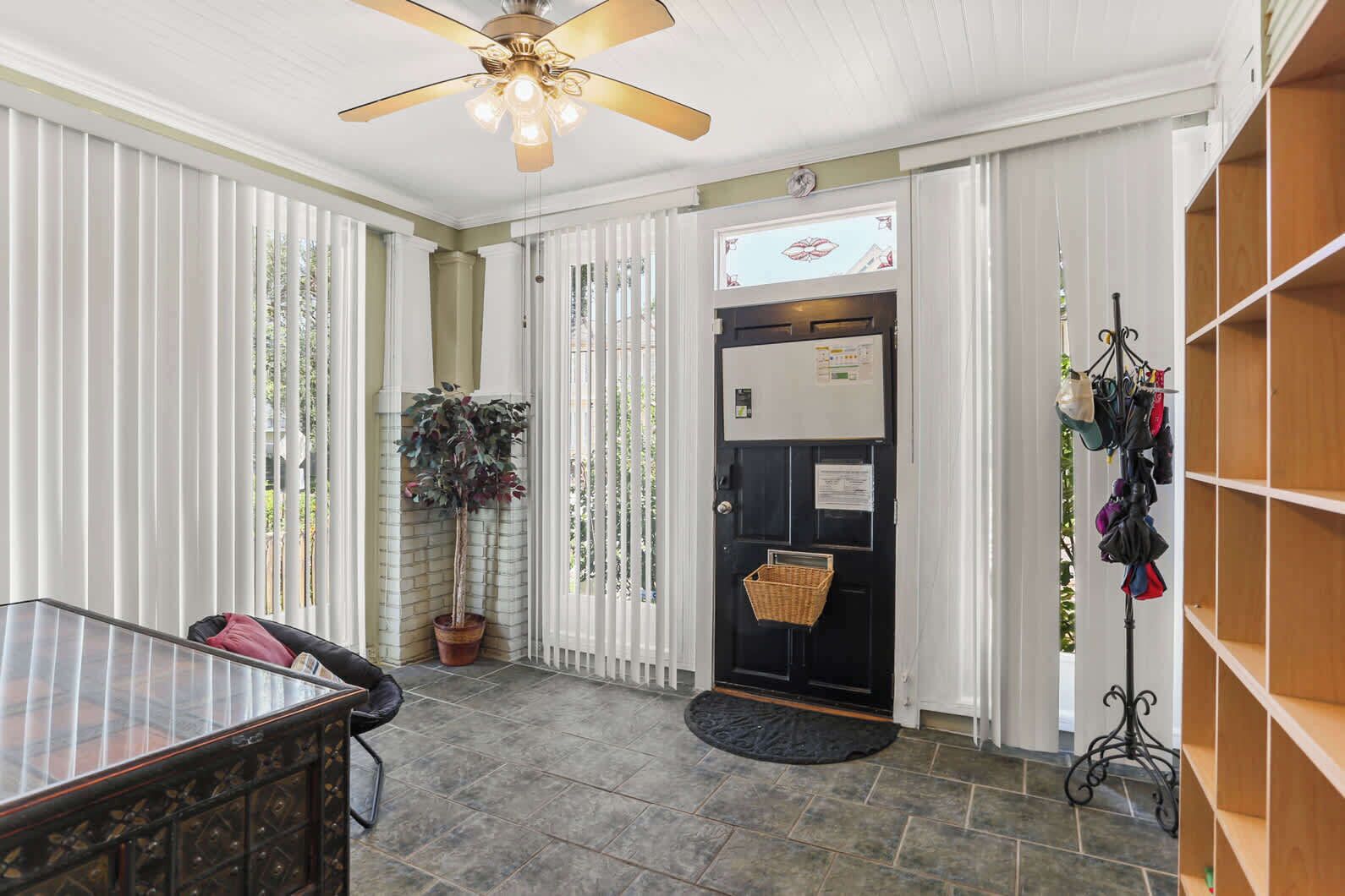 A room with a ceiling fan, a potted plant, a door with a basket, and a chair.