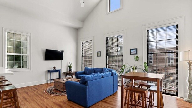 Un salón amplio con un sofá azul, una mesa de comedor de madera y taburetes de bar.