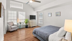 Un dormitorio con cama, una silla, televisor, cómoda y ventilador de techo.