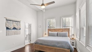 A bedroom with a wooden bed, white walls, and a ceiling fan. - Modern 2BR | Garden District | Stunning Luxury (New Orleans)