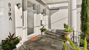 A modern building with a white brick exterior, numbered 839A, featuring large glass doors, potted plants, and a stone-tiled entrance area. - Modern 2BR | Garden District | Stunning Luxury (New Orleans)