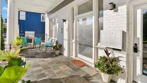 A covered patio with a blue wall, potted plants, and a seating area with chairs. - Modern 2BR | Garden District | Stunning Luxury (New Orleans)