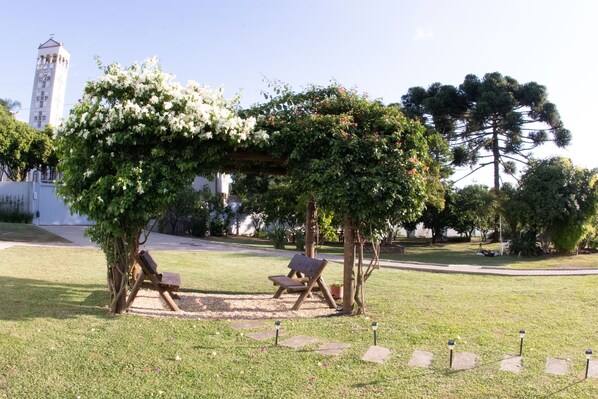 Un jardín con un pabellón, un banco, un césped cuidado y un gran árbol.