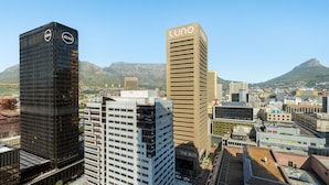 A cityscape with prominent buildings including a tall black building with 'absai' logos, a beige building with 'LUNO' signage, and a building labeled 'THE BOX'.