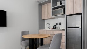 A modern kitchen with a round wooden table, two grey chairs, a stainless steel refrigerator, and wooden cabinets.