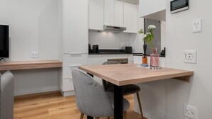 A modern kitchen with white cabinets, a wooden dining table, and a grey chair. - Stunning Central Studio at The Carrington (Cape Town)