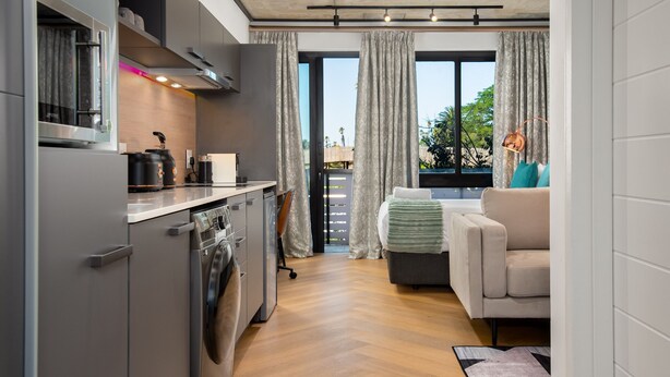 Eine kompakte Küche mit modernen Geräten, ein Essbereich mit einer Couch und Blick durch große Fenster.