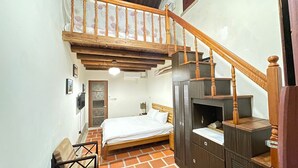 Un dormitorio con cama de madera, un escritorio pequeño, una silla, un armario y una escalera.