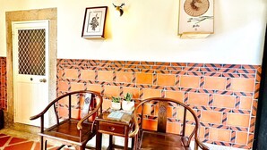 Una habitación con dos sillas de madera, una mesita, una puerta con mosquitera y un pared de azulejos con diseño geométrico.
