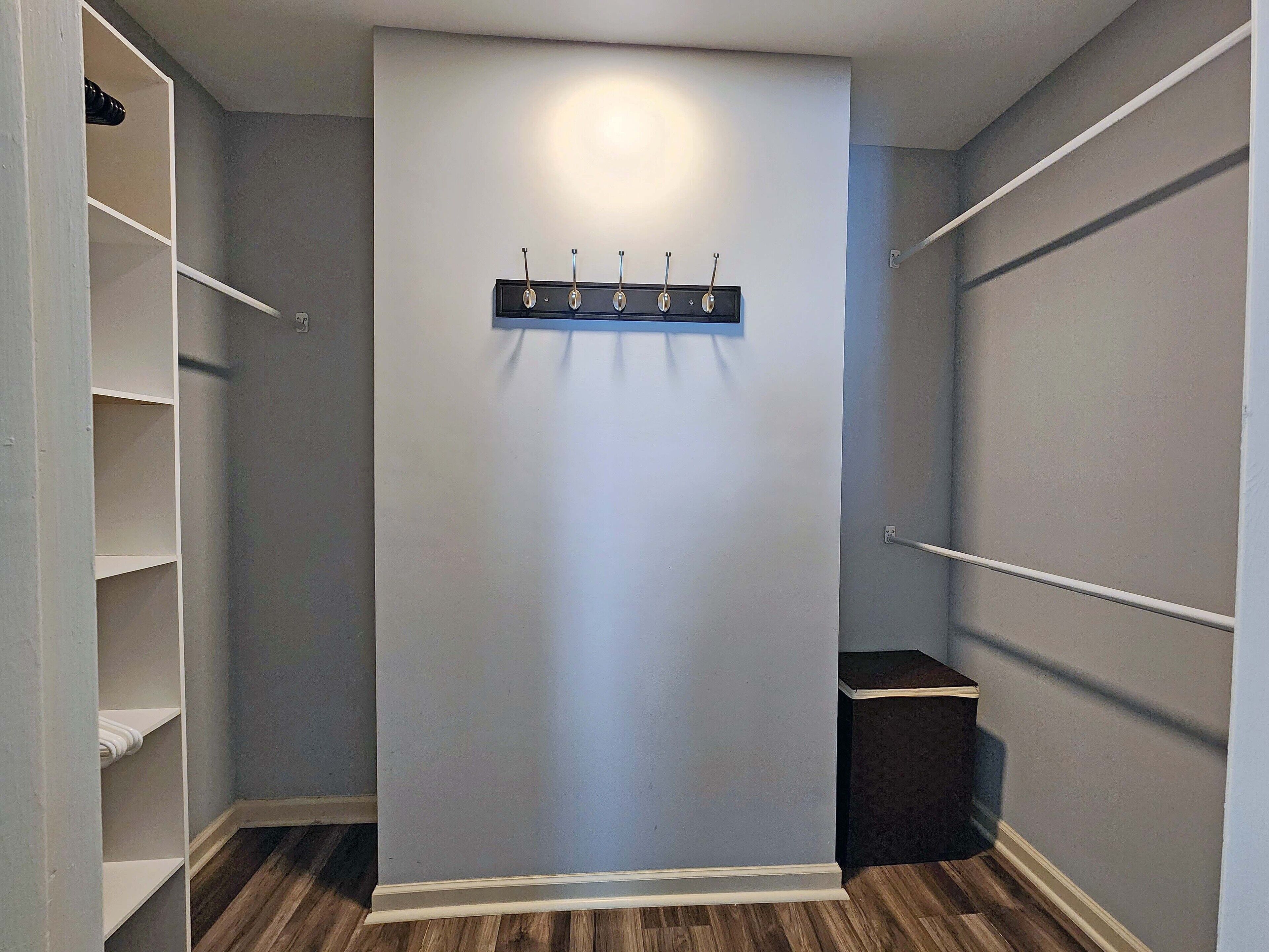 Un dressing avec un porte-manteau central, un plancher en bois et des murs gris.