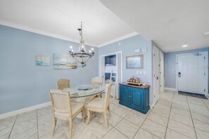 A dining area with a glass table, wicker chairs, a chandelier, and a blue cabinet with decorative items.
