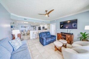 A modern living room with a blue sofa, a white armchair, a coffee table, and a television mounted on the wall.