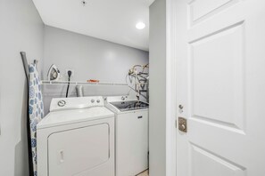 Ein Waschraum mit einer Waschmaschine und einem Trockner mit Frontlader, einem Wäscheständer und einem Dampfbügeleisen an der Wand.