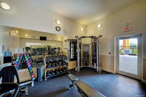 Ein Fitnessraum mit unterschiedlichen Trainingsgeräten, einer Bank und einem Wasserspender.