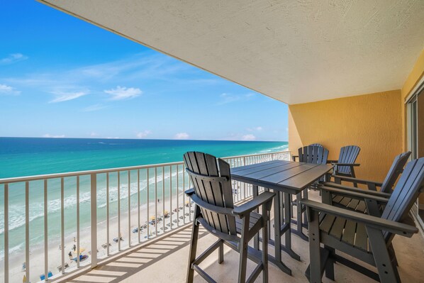 A balcony with a view of the ocean, a table, and chairs.