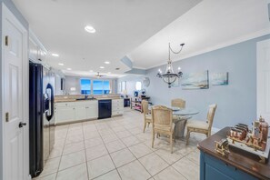 A spacious kitchen with a central island, a dining area with a round table, and a view through the window.