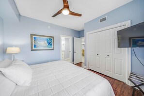 Une chambre à coucher avec un lit, un ventilateur de plafond, un tableau, une télévision et une armoire.