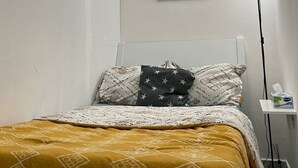 Una habitación pequeña y poco amueblada con una cama, una mesita de noche y una lámpara de pared.
