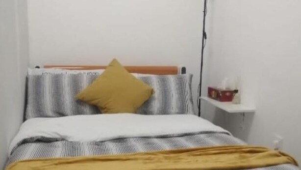 Un dormitorio sencillo con una cama, una mesita de noche, una lámpara y un estante pequeño.