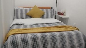 Un dormitorio con cama, mesita de noche, lámpara y un cuadro colgado en la pared.